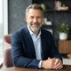 A professional portrait of a smiling, diverse man with a groomed beard, captured in a bright, modern setting.
