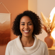 A smiling woman in her late 20s to early 30s looks directly at the camera, with a warm-toned background.